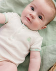 Un bébé allongé dans un panier en rosier portant le Body bébé Samé de la marque Bobo Bassari, avec un design inspiré de motifs africains, en coton doux, adapté pour les nouveaux-nés.