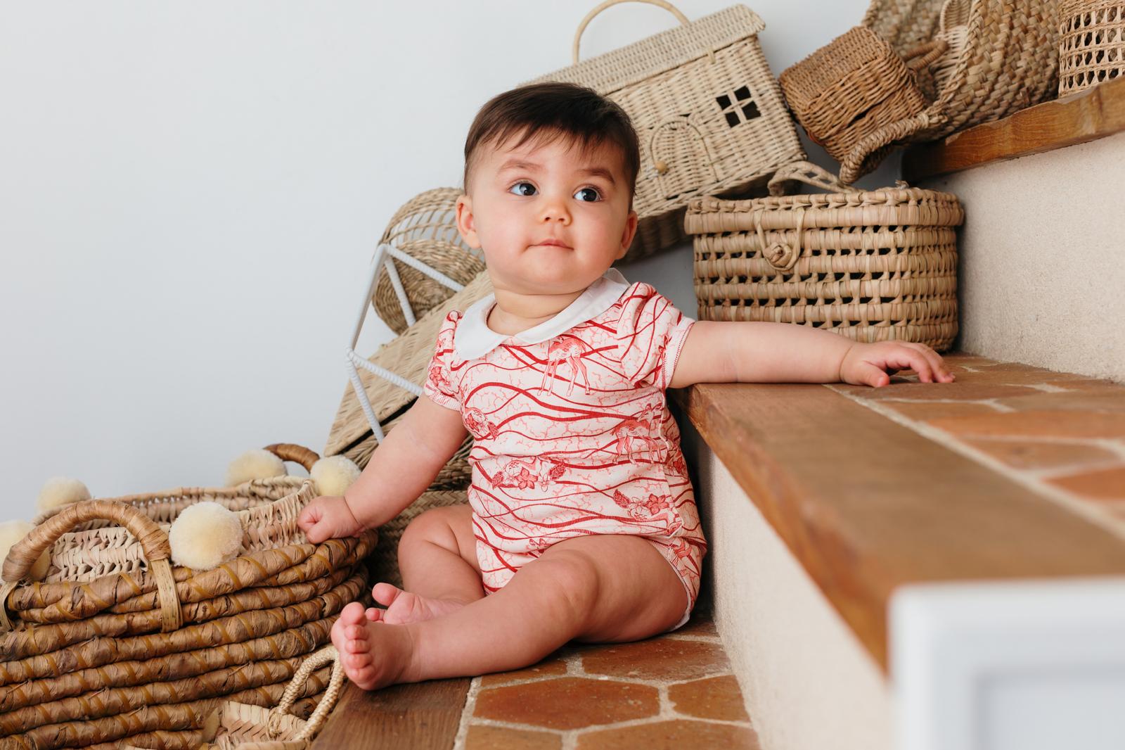 Bébé assis sur des marches en extérieur, portant le body bébé imprimé Bandia de Bobo Bassari, conçu avec un tissu doux et un design inspiré des motifs africains