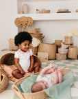 Deux bébés portant des tenues Bobo Bassari : l'un assis avec le body bébé col imprimé Bandia, l'autre allongé dans un panier en rotin, entouré d'une ambiance chaleureuse et naturelle