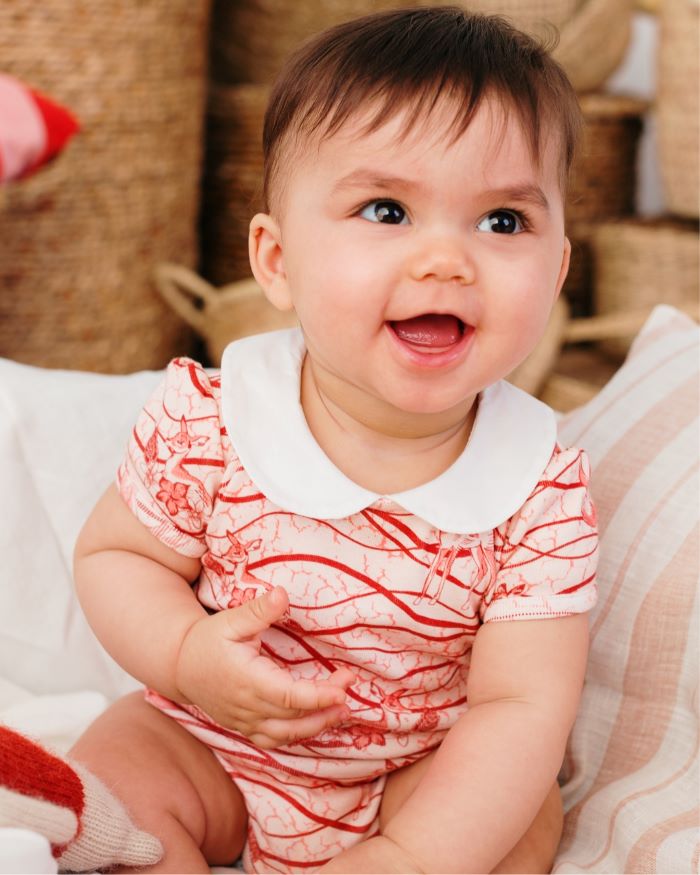 Un bébé tout sourire portant un body imprimé Bandia de Bobo Bassari, une tenue confortable et colorée inspirée de l'héritage africain, idéale pour les tout-petits