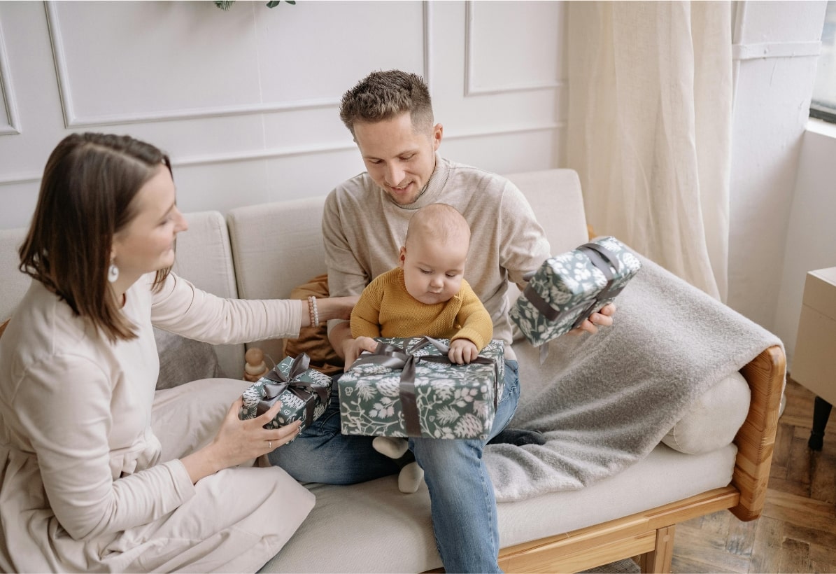 Un couple rayonnant déballant un cadeau de naissance avec leur bébé, illustrant un moment de joie et de partage familial